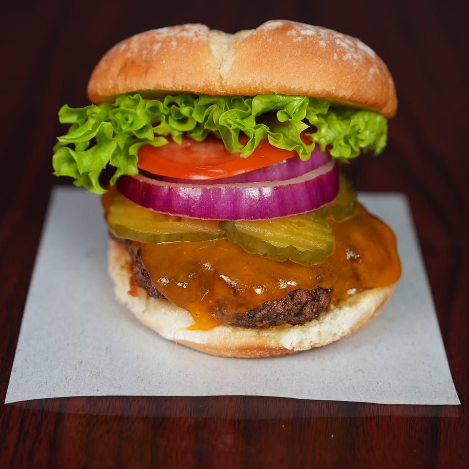 Close-up of a cheeseburger with lettuce, tomato, red onion, pickles, and melted cheese on a bun.