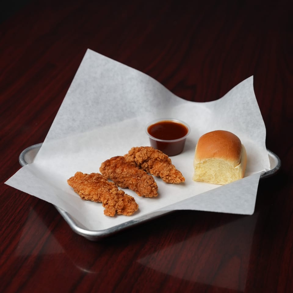 Crispy fried chicken strips with a soft dinner roll and dipping sauce on a paper-lined metal tray.